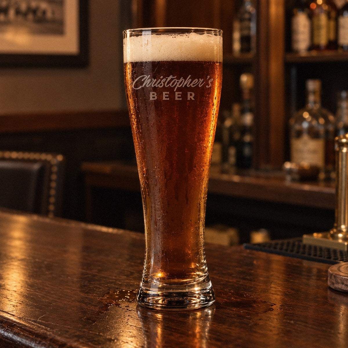 Big Boy 22 oz personalized pilsner glass etched Christopher's in script with BEER below, filled with amber beer on a home bar