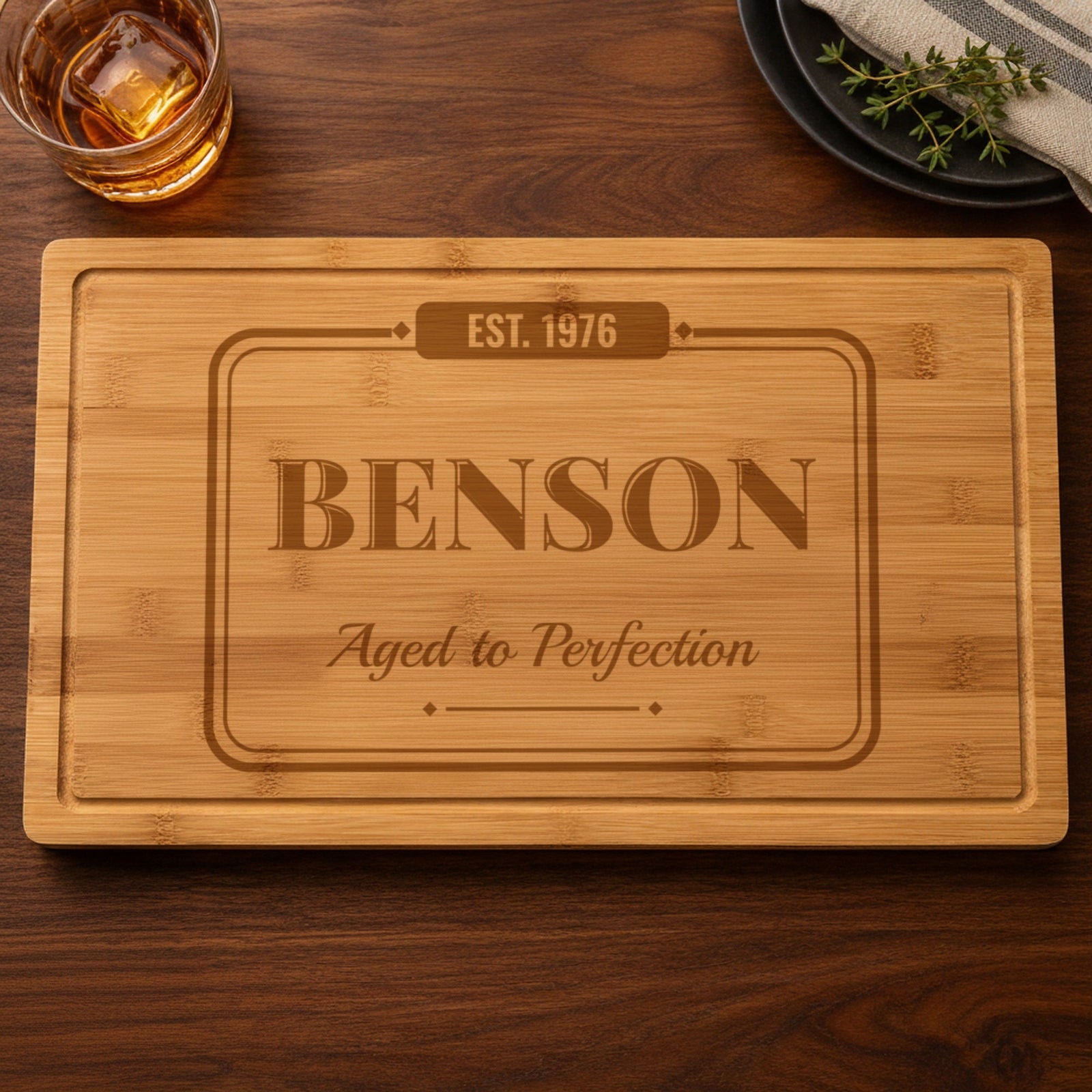 Personalized birthday cutting board engraved with EST. 1976, the name Benson and Aged to Perfection in a vintage pub sign frame on bamboo
