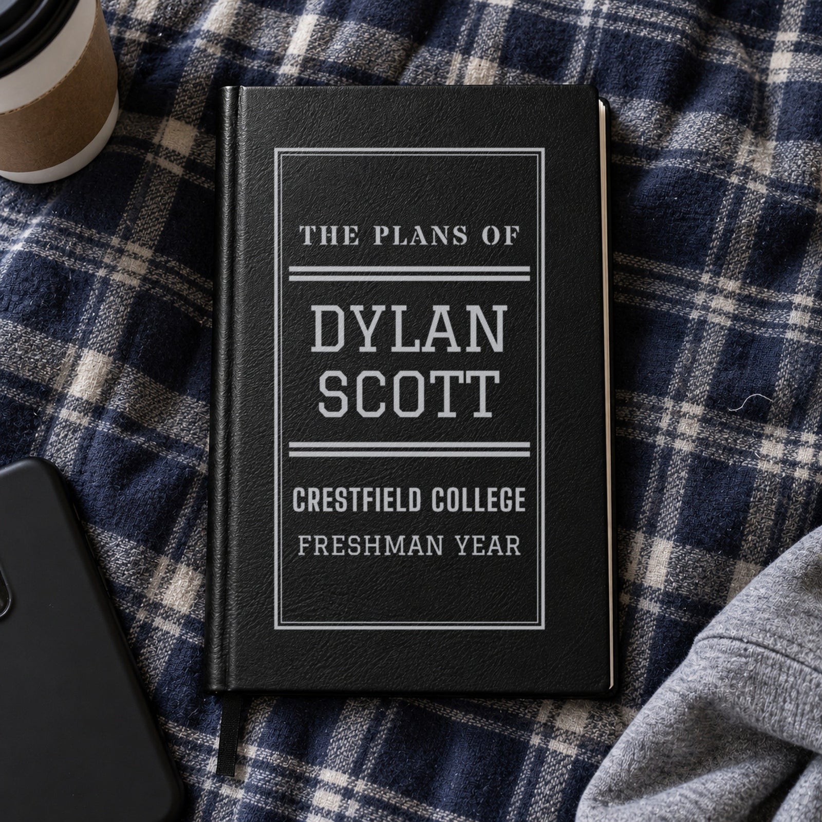 Black journal engraved in silver: The Plans Of Dylan Scott, Crestfield College, Freshman Year, on a plaid dorm comforter, a personalized gift for a son in college