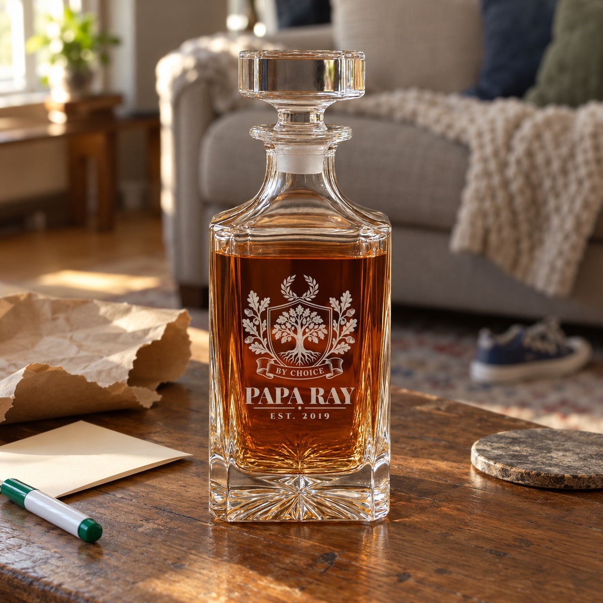 Bonus dad decanter from the kids on a living room coffee table with torn kraft wrapping paper and a folded card, engraved Papa Ray, Est. 2019