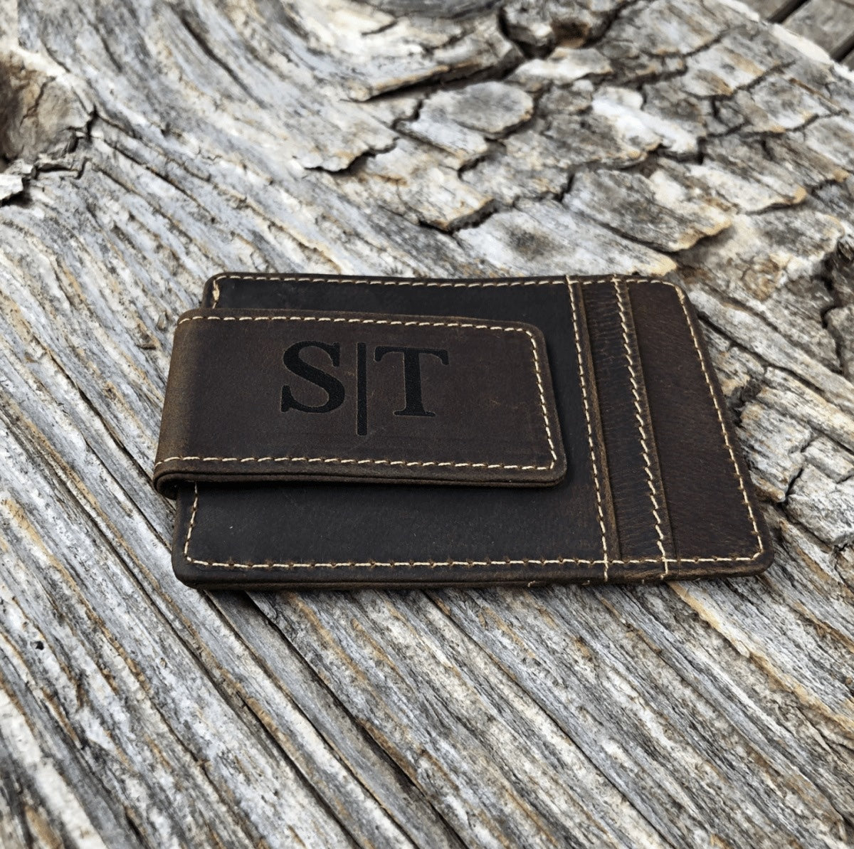 Real photo of the Classic Leather Money Clip on weathered wood, the magnetic clip engraved with the initials S and T in a serif