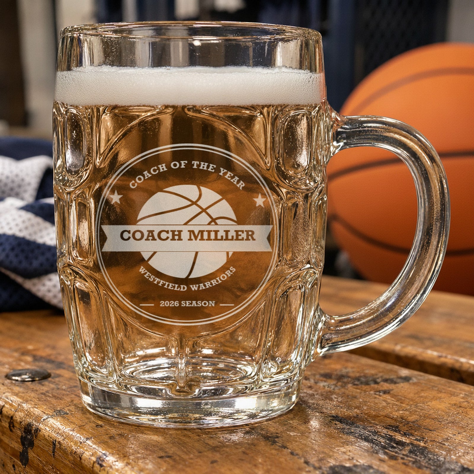 Personalized basketball coach beer stein on a locker room bench beside an orange basketball, frosted engraving reading Coach of the Year, Coach Miller and Westfield Warriors