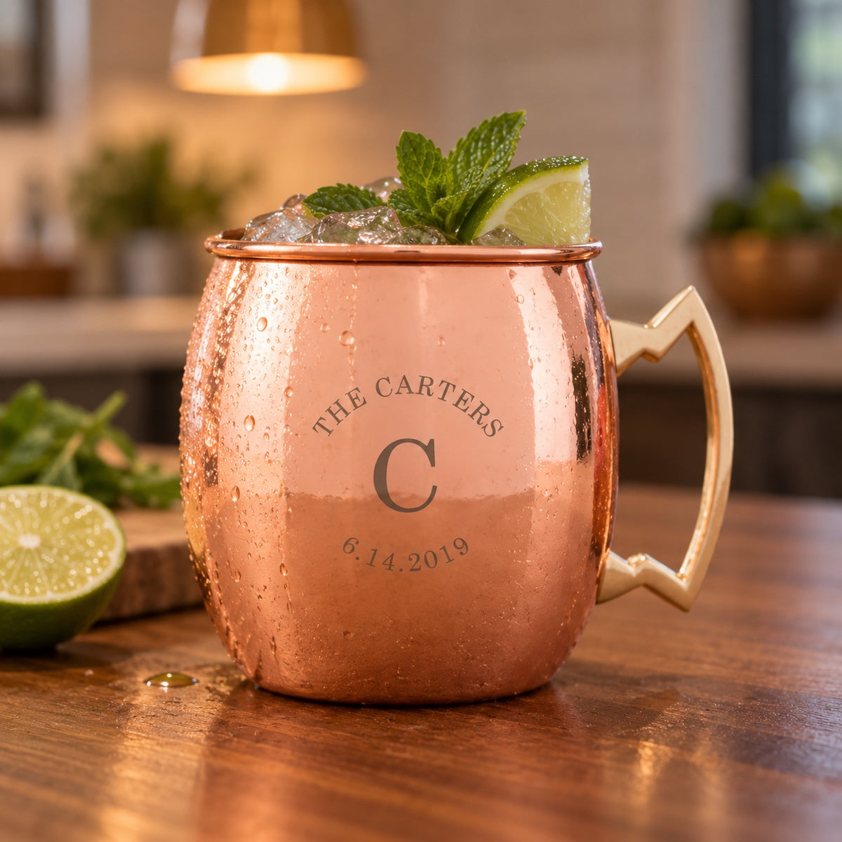Couple's copper Moscow mule mug engraved THE CARTERS arched over a large C initial and the date 6.14.2019, filled with a mule, lime and mint on a kitchen island.