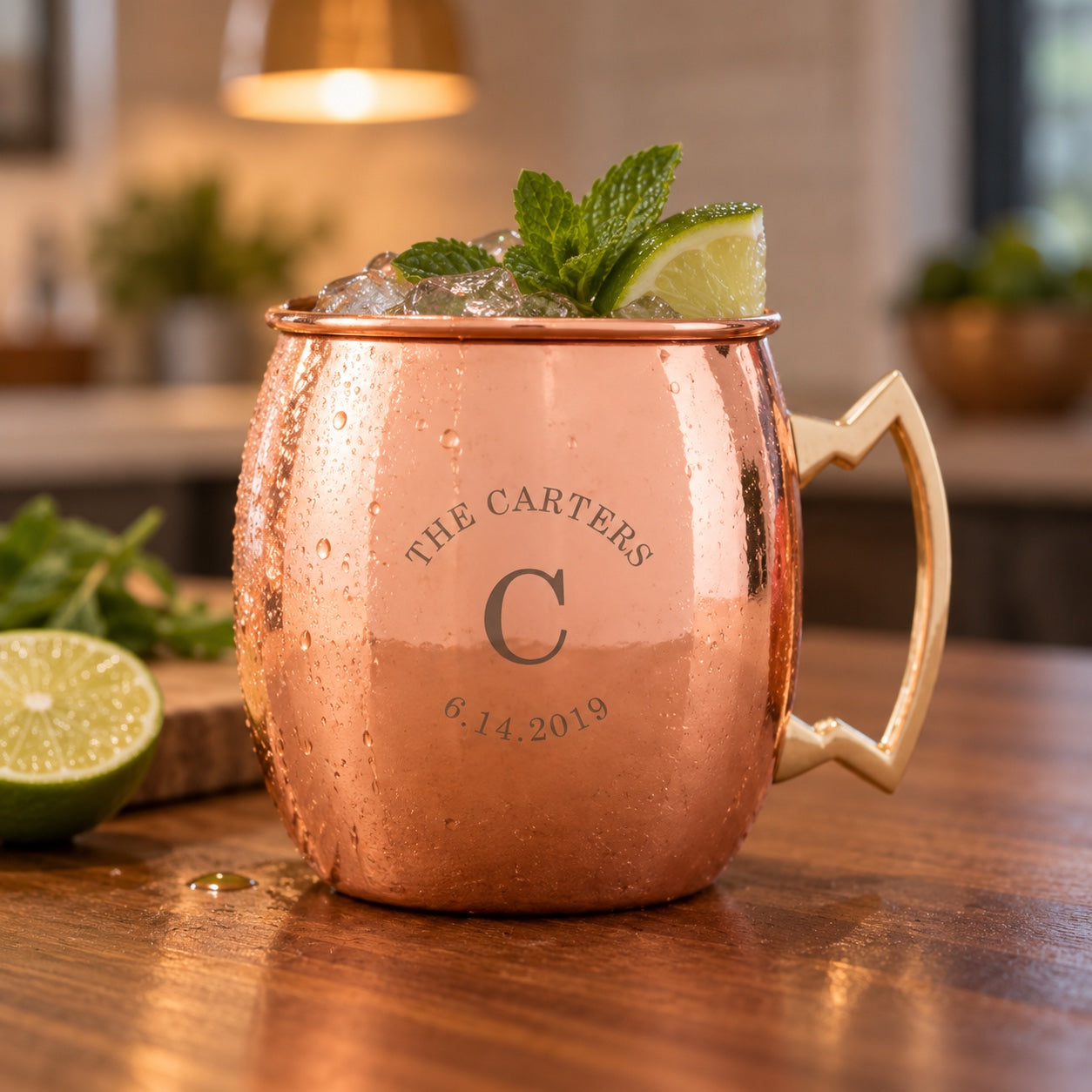 Couple's copper Moscow mule mug engraved THE CARTERS arched over a large C initial and the date 6.14.2019, filled with a mule, lime and mint on a kitchen island.