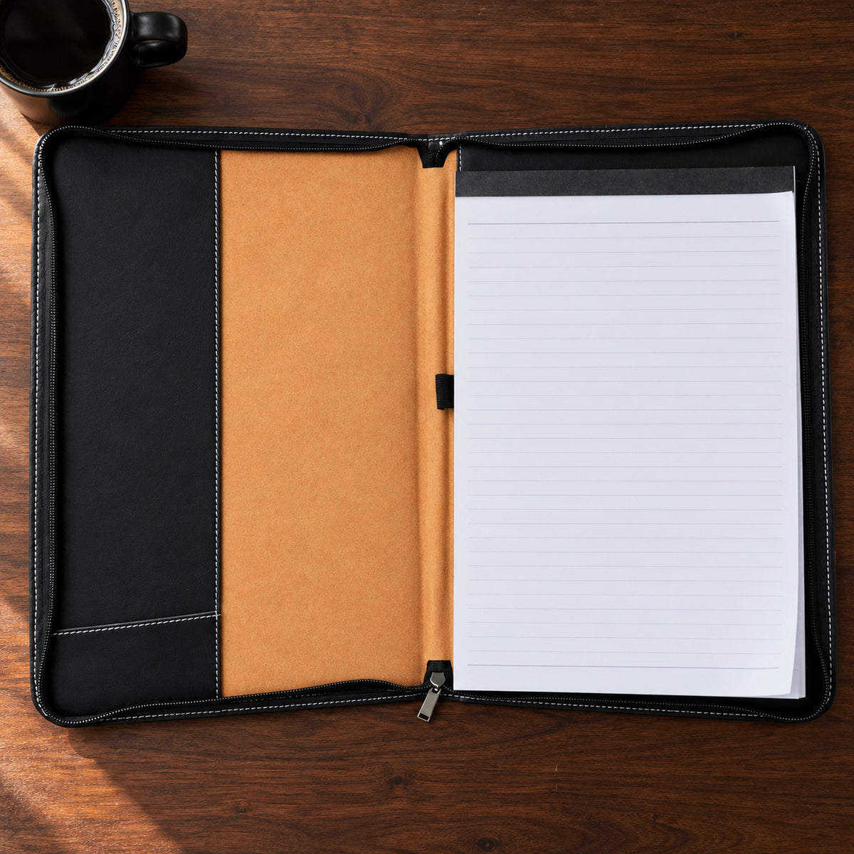 Inside the black zip padfolio: a lined legal pad on the right, an empty elastic pen loop on tan lining and a tall pocket on the left