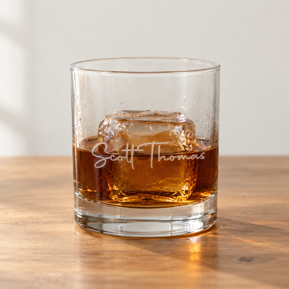 Custom man myth legend whiskey glass engraved with the name Scott Thomas in script, a pour of bourbon over a large ice cube