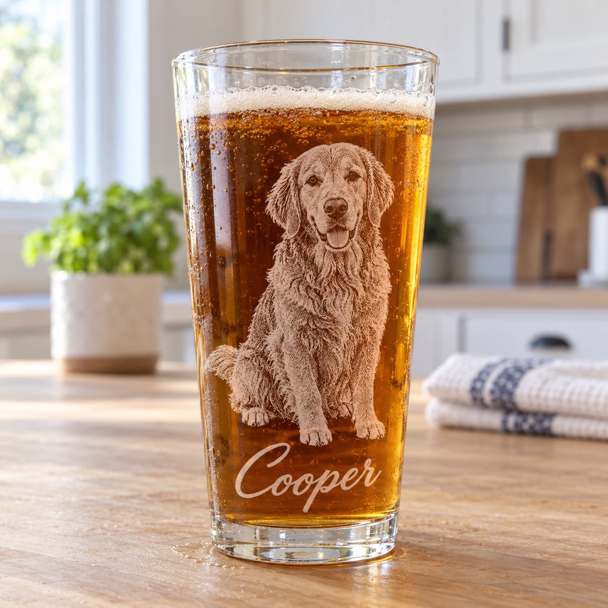 Custom pet pint glass engraved with a golden retriever portrait and the name Cooper, filled with beer on a bright kitchen counter