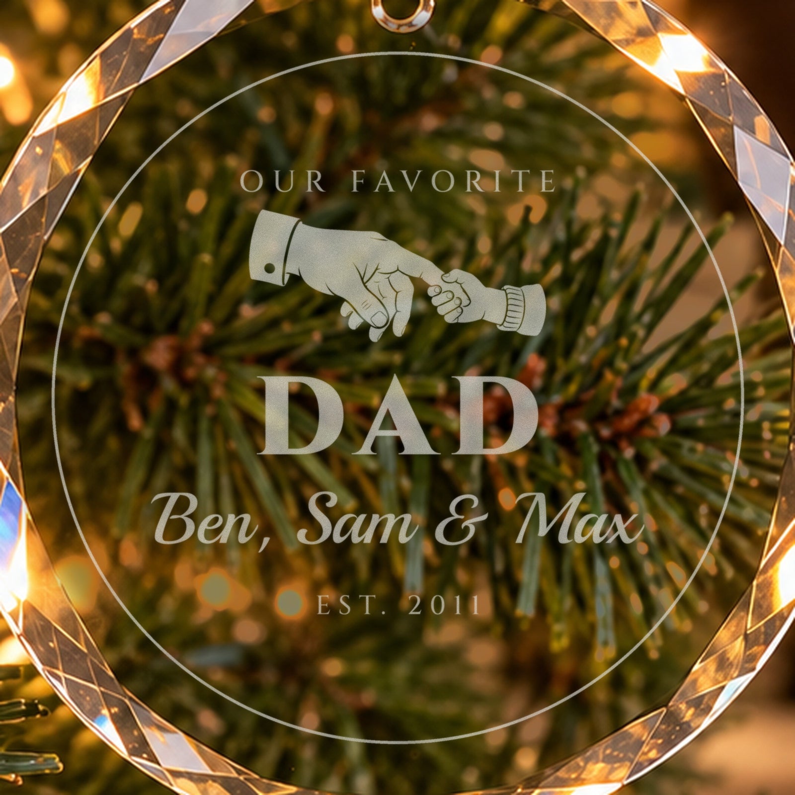 Close-up of the frosted engraving on the dad ornament: a big hand holding a little one, OUR FAVORITE DAD, Ben, Sam & Max and EST. 2011