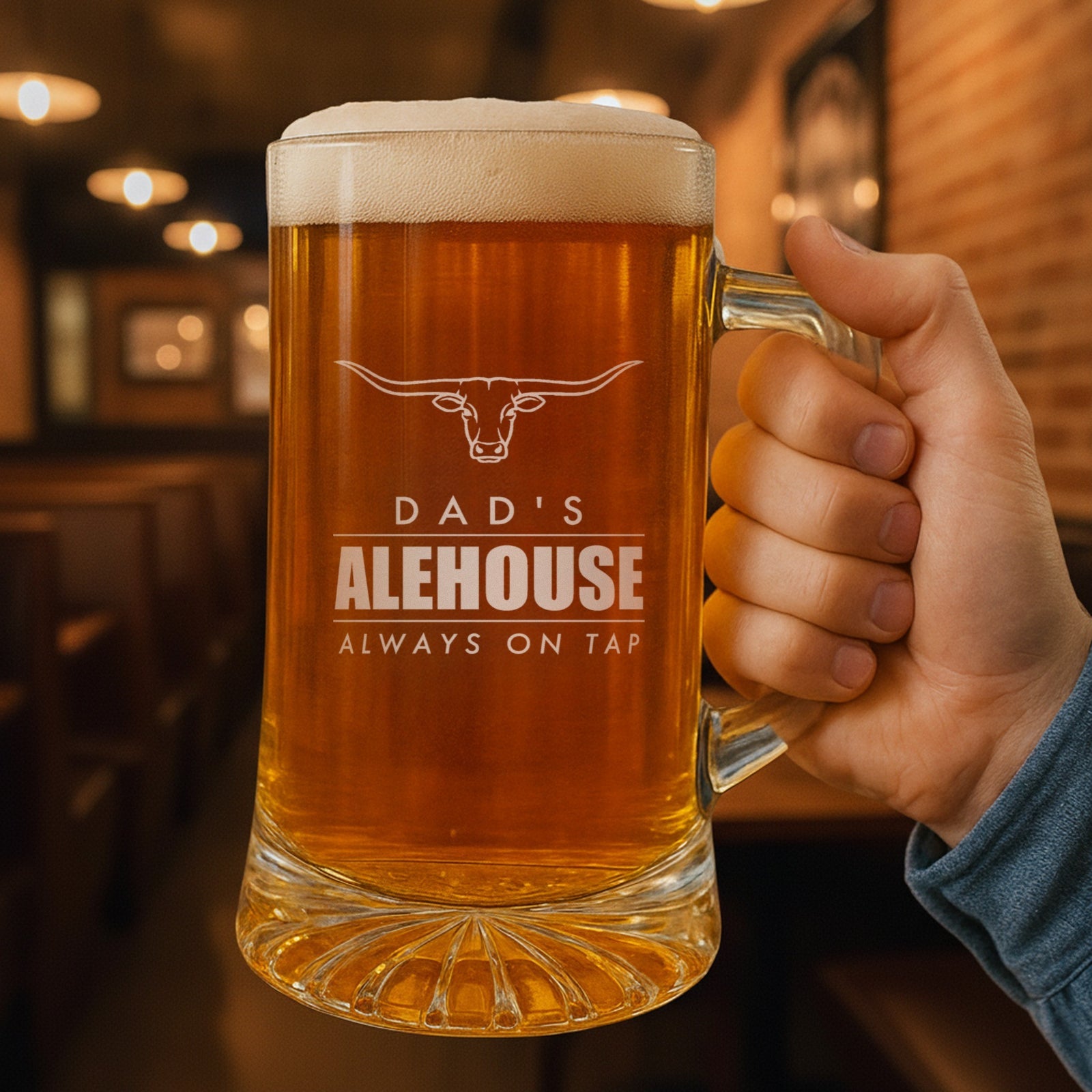 Hand holding a 25 oz personalized beer stein in a pub, engraved with a longhorn and the lines Dad's, Alehouse and Always on Tap
