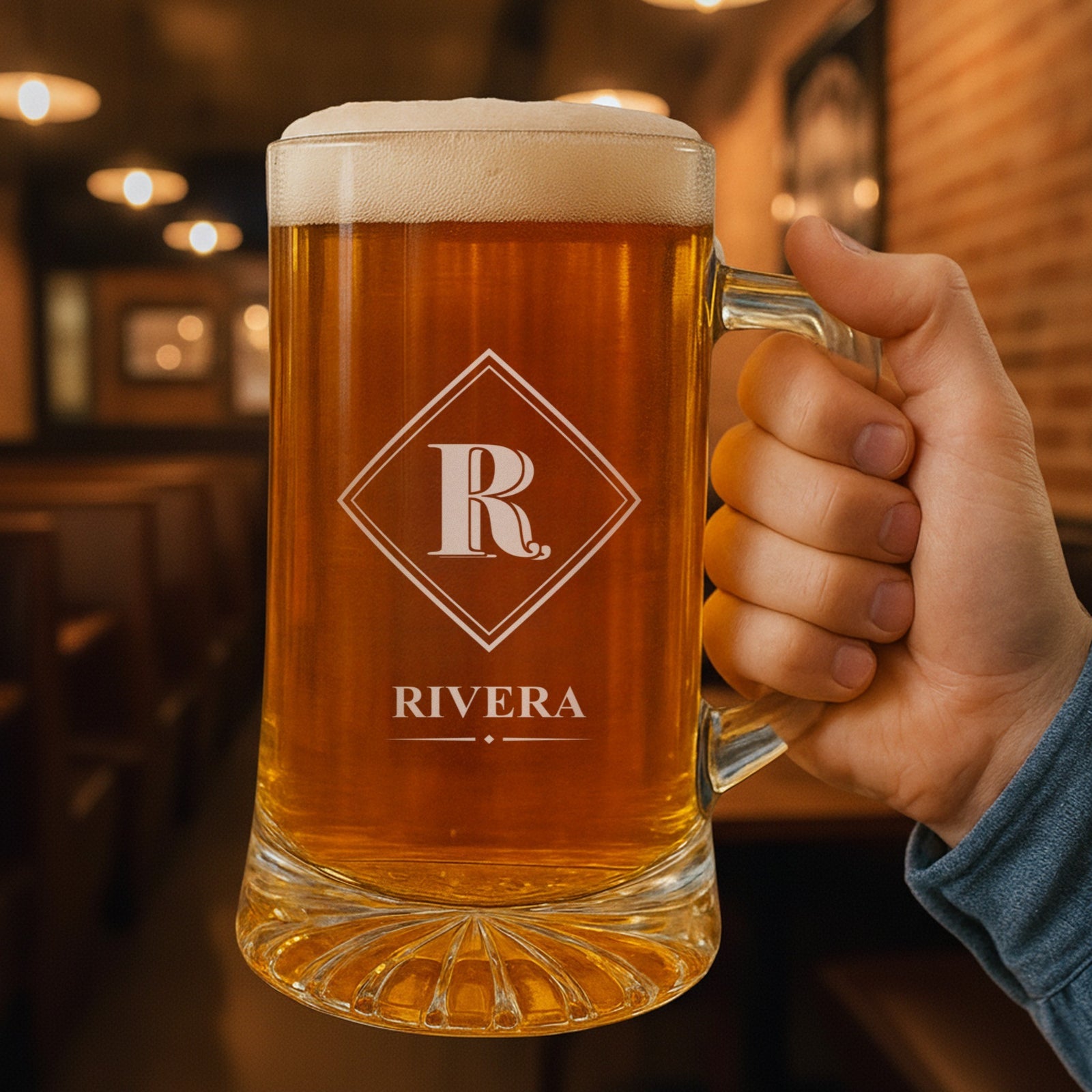 Hand holding a personalized beer stein in a pub, engraved with the Diamond Frame monogram design showing the initial R above the last name Rivera