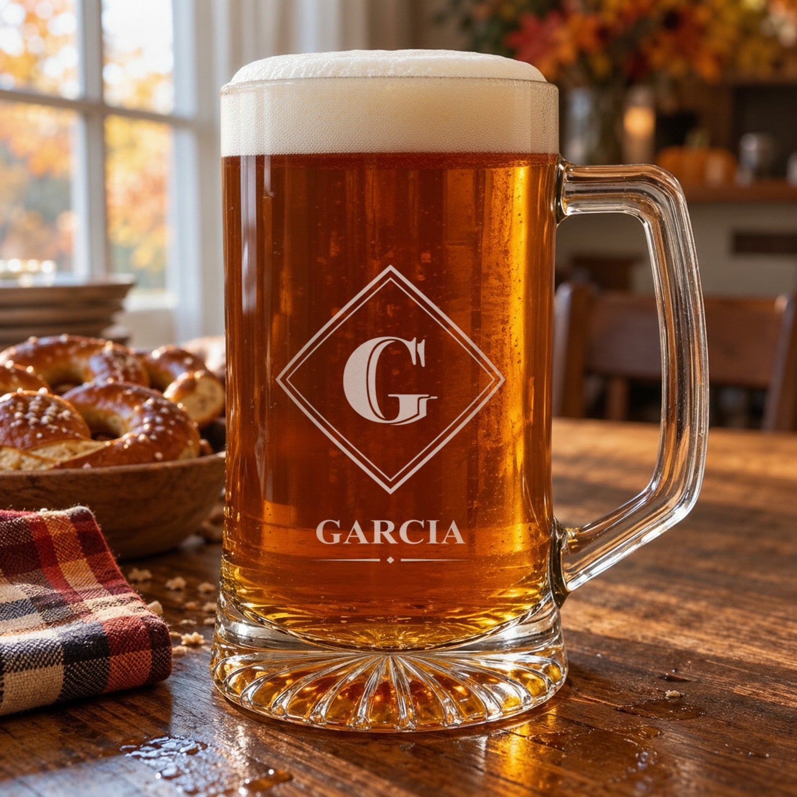 Engraved glass beer stein of amber lager on an autumn kitchen table, personalized with the Diamond Frame monogram showing G and the last name Garcia