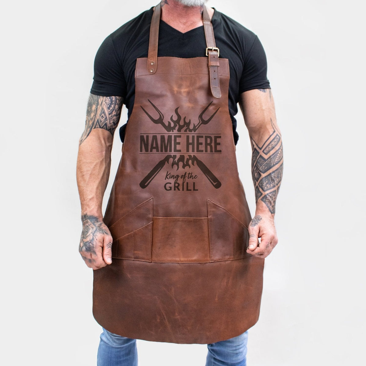 Personalized brown full-grain leather barbecue apron with front pocket and adjustable straps.
