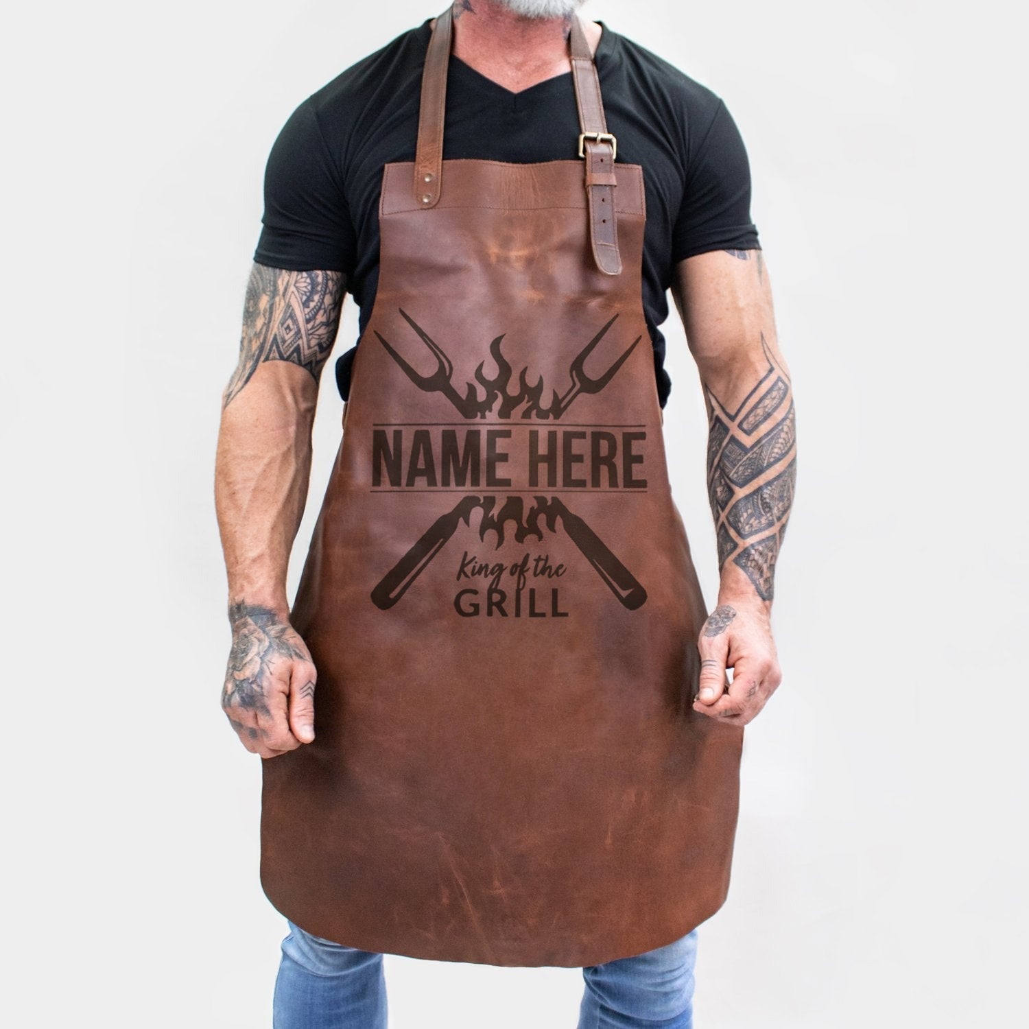 Personalized brown full-grain leather barbecue apron with front pocket and adjustable straps.