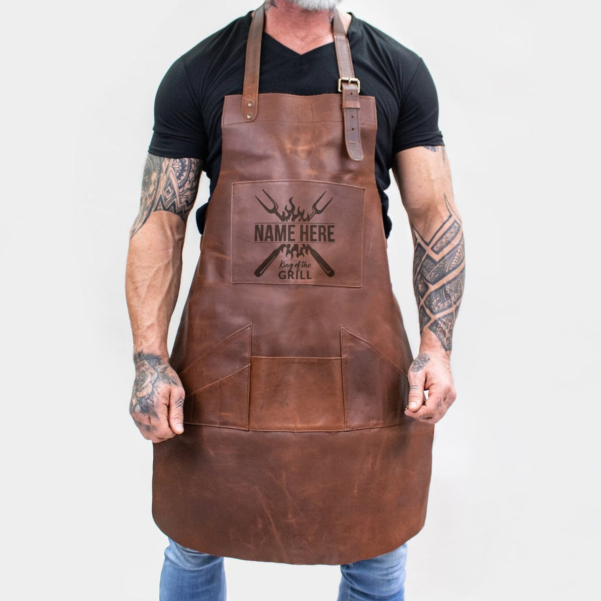 Personalized brown full-grain leather barbecue apron with front pocket and adjustable straps.