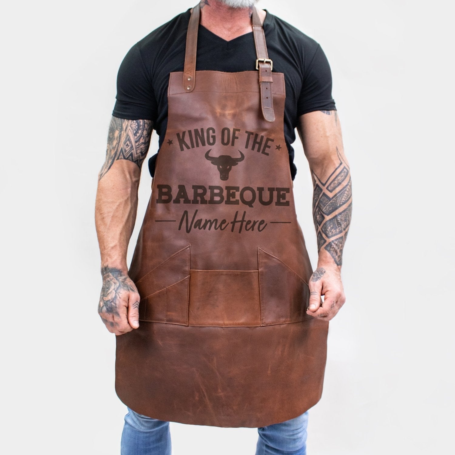 Personalized brown full-grain leather barbecue apron with front pocket and adjustable straps.