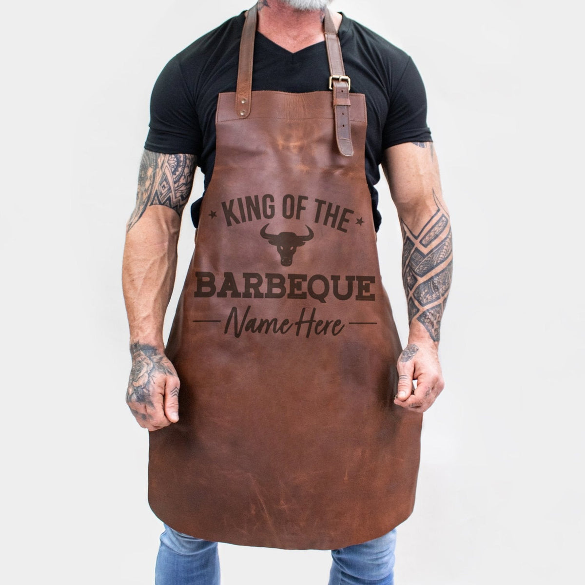 Personalized brown full-grain leather barbecue apron with front pocket and adjustable straps.