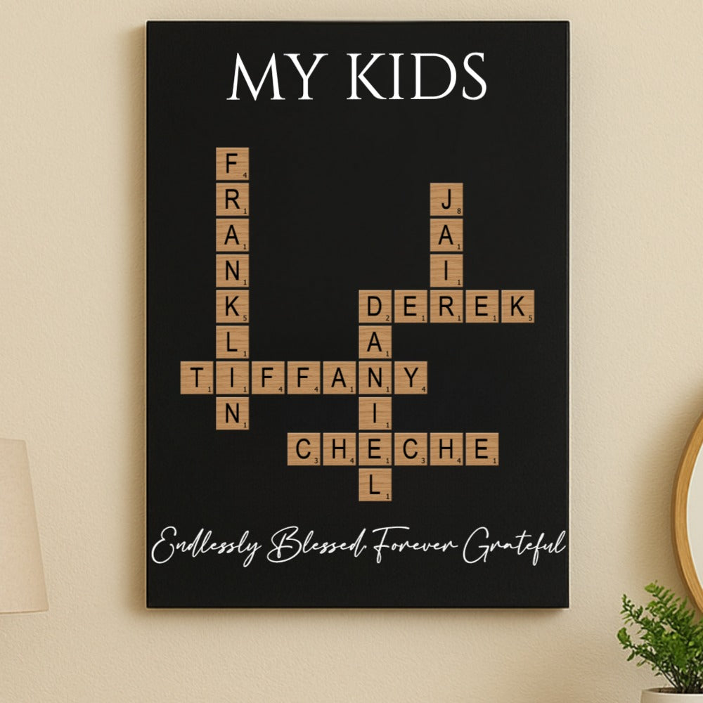 Black wall sign with "MY KIDS" at top and Scrabble-style tiles arranged in crossword pattern displaying sample names Frank, Tiffany, Derek, and Cheche, with script text at bottom reading "Endlessly Blessed Forever Grateful