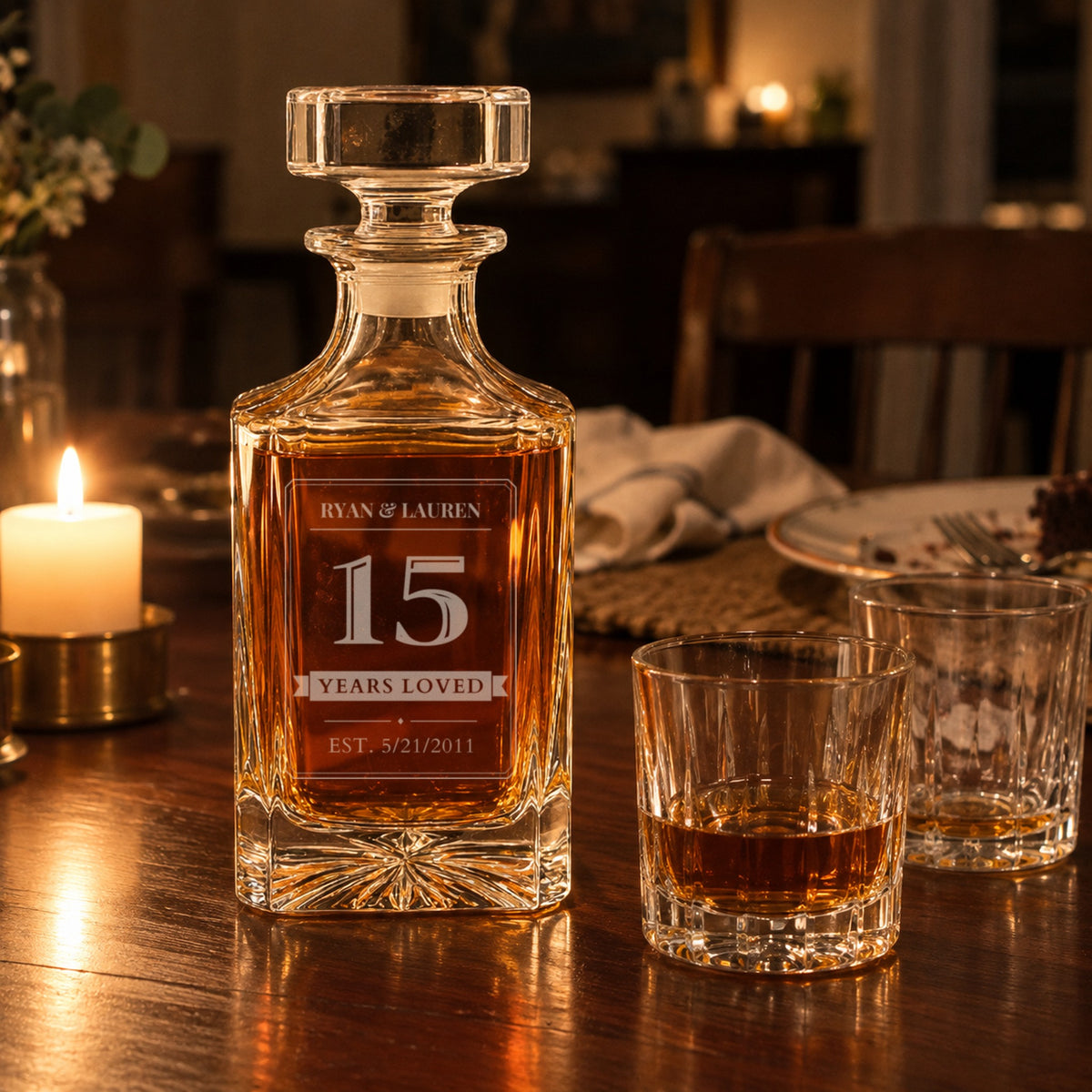Engraved 15 year anniversary gift for him on a candlelit dinner table, decanter reading Ryan and Lauren, 15, Years Loved, EST. 5/21/2011, beside two rocks glasses