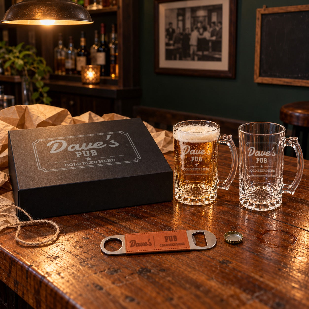 Engraved beer mug gift set in a home basement bar: gift box, one full and one empty glass mug and a bottle opener, all reading Dave's Pub Cold Beer Here