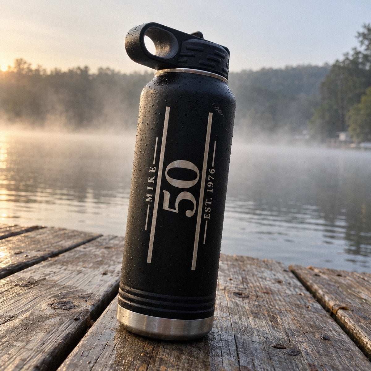Engraved birthday water bottle for men with MIKE, a large 50 and EST. 1976 running up a 32 oz matte black bottle on a misty lake dock
