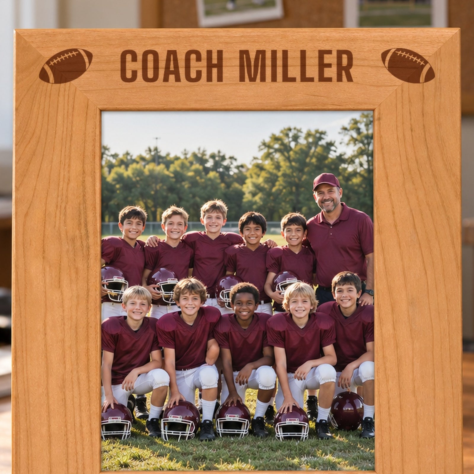 Close-up of Coach Miller laser engraved in bold capitals between two footballs on the top border of a red alder coach picture frame