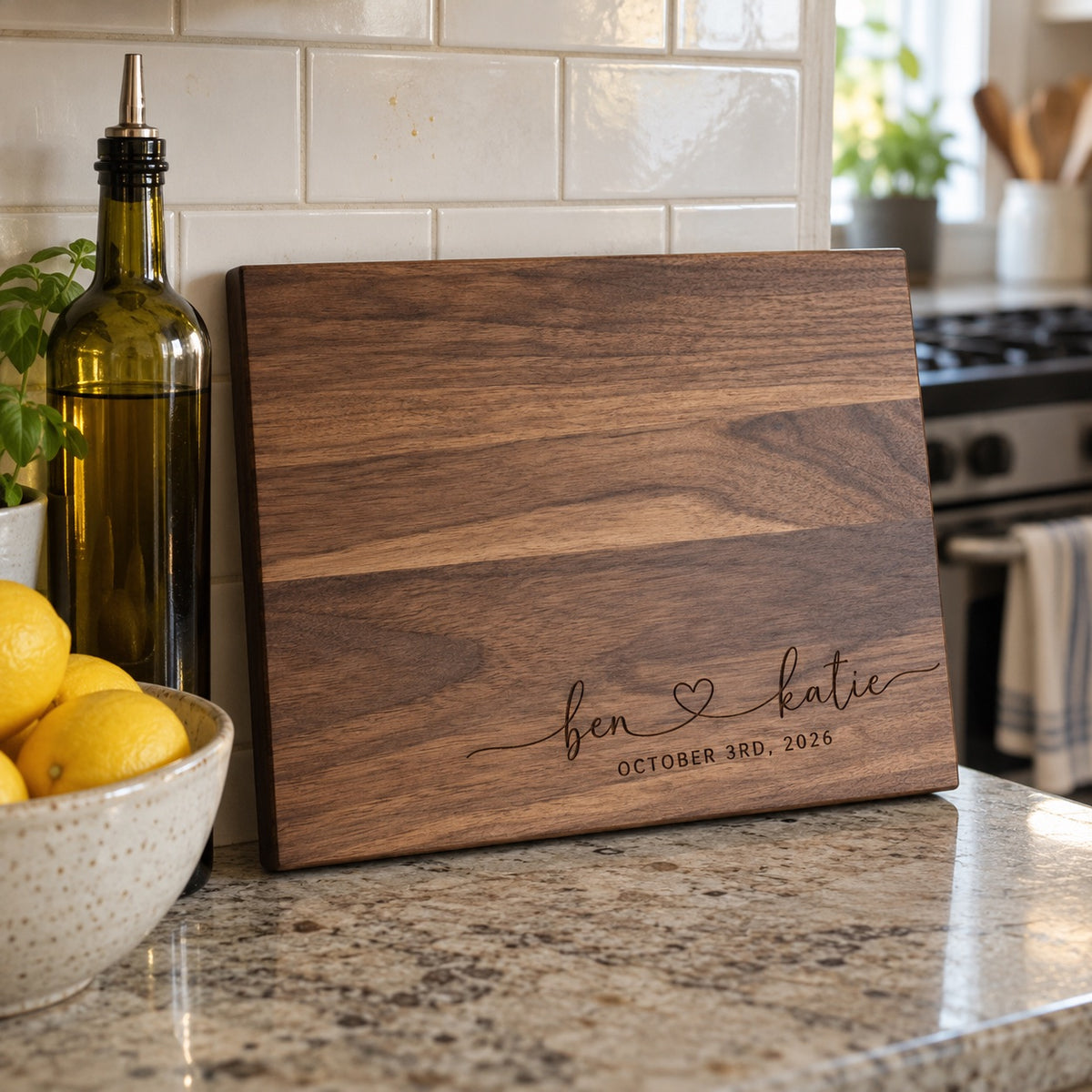 Walnut couples cutting board engraved ben and katie with OCTOBER 3RD, 2026 leaning on a kitchen backsplash beside olive oil and a bowl of lemons
