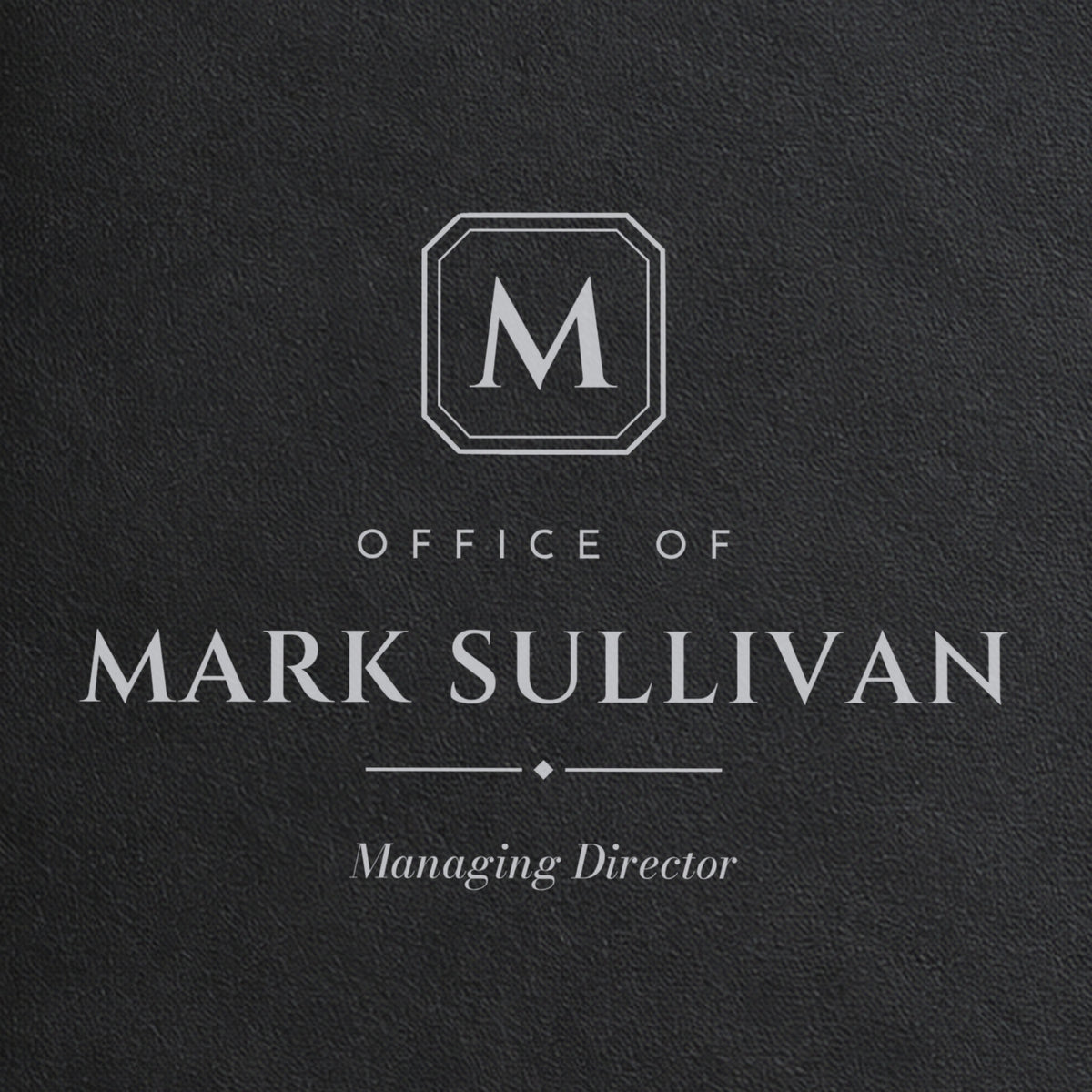 Close-up of the silver laser engraving on the black padfolio: M monogram plate, Office of, Mark Sullivan and Managing Director in italic