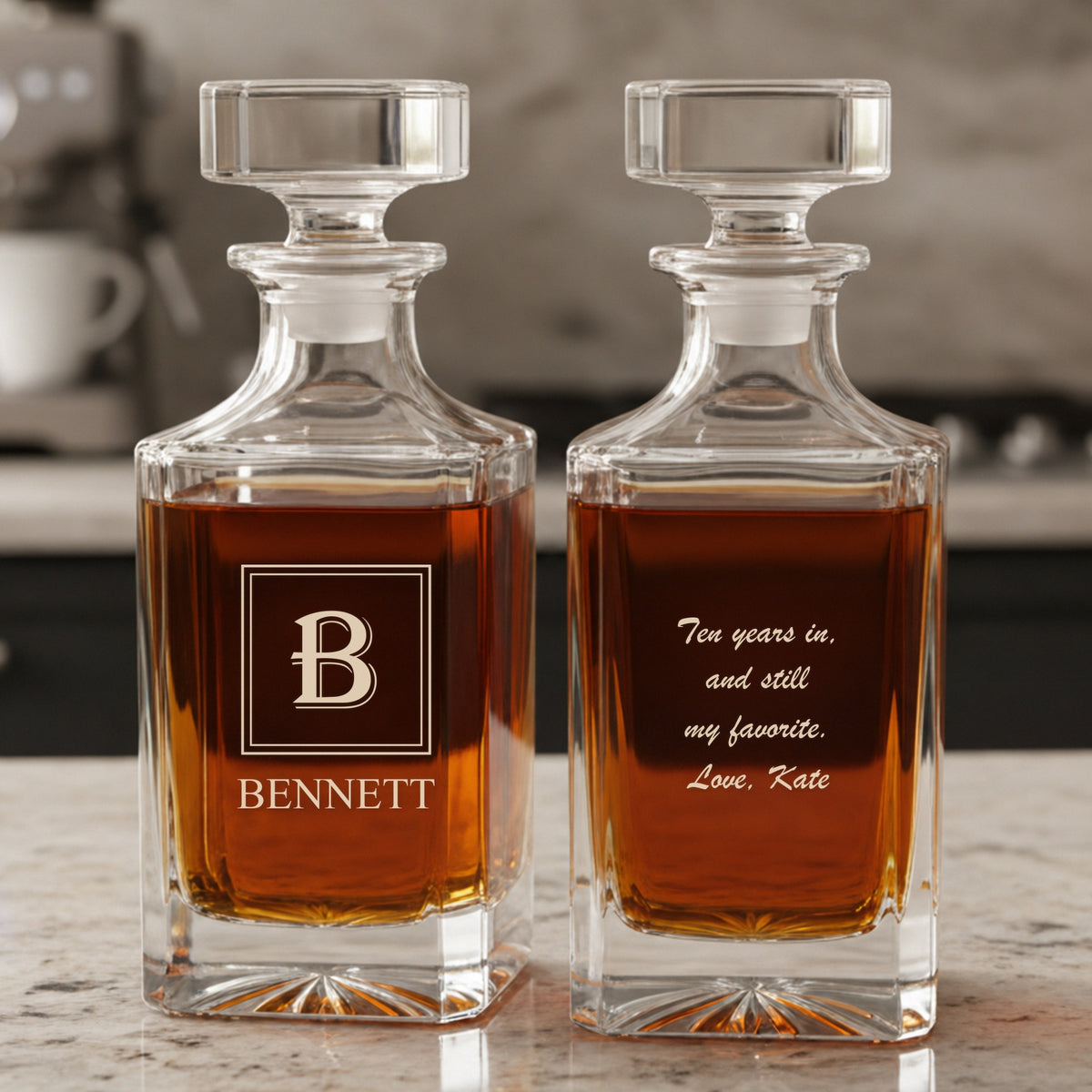 Two engraved whiskey decanters on a marble kitchen counter, one with a B monogram and the name BENNETT, one with an anniversary note from Kate on the back