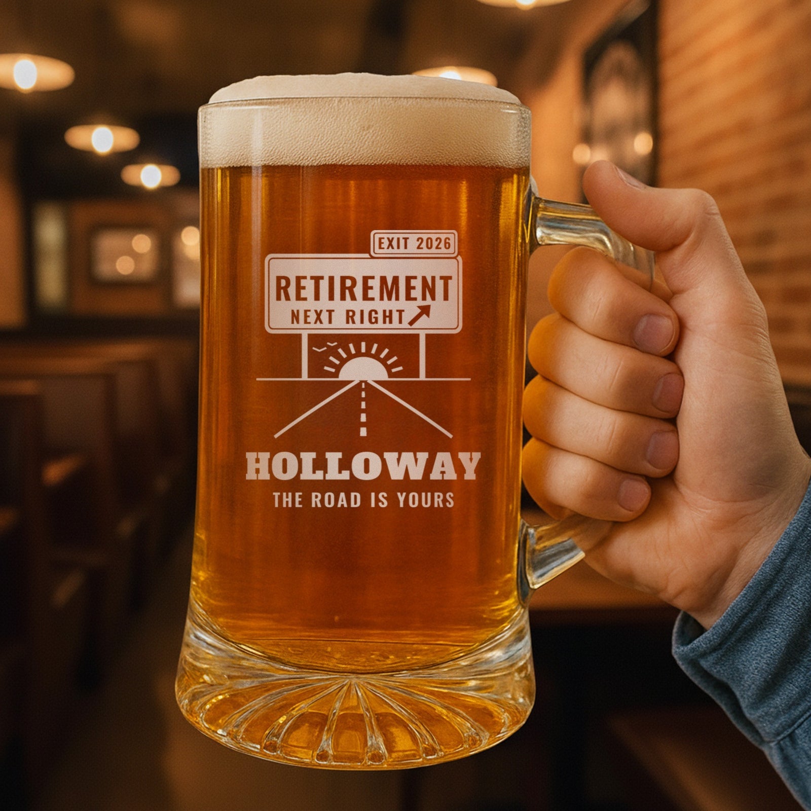 Hand holding the personalized exit sign retirement beer mug in a pub, engraved EXIT 2026, RETIREMENT NEXT RIGHT, HOLLOWAY and THE ROAD IS YOURS