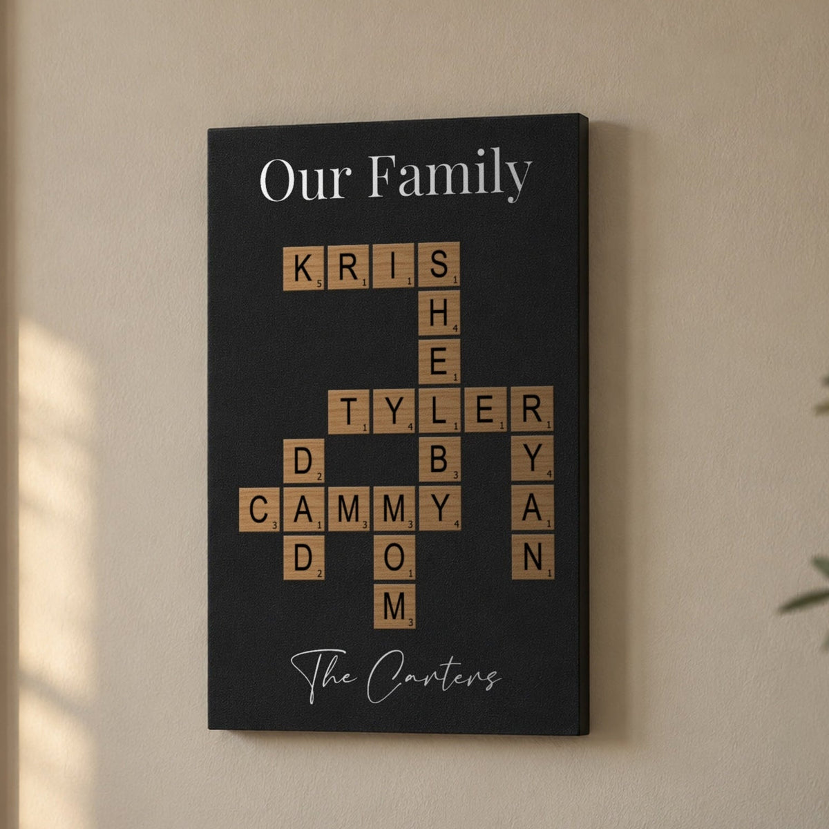 Family crossword wall art on a living room wall, Our Family title over wood-tone letter tiles spelling Kris, Shelby, Tyler, Ryan, Dad, Cammy and Mom