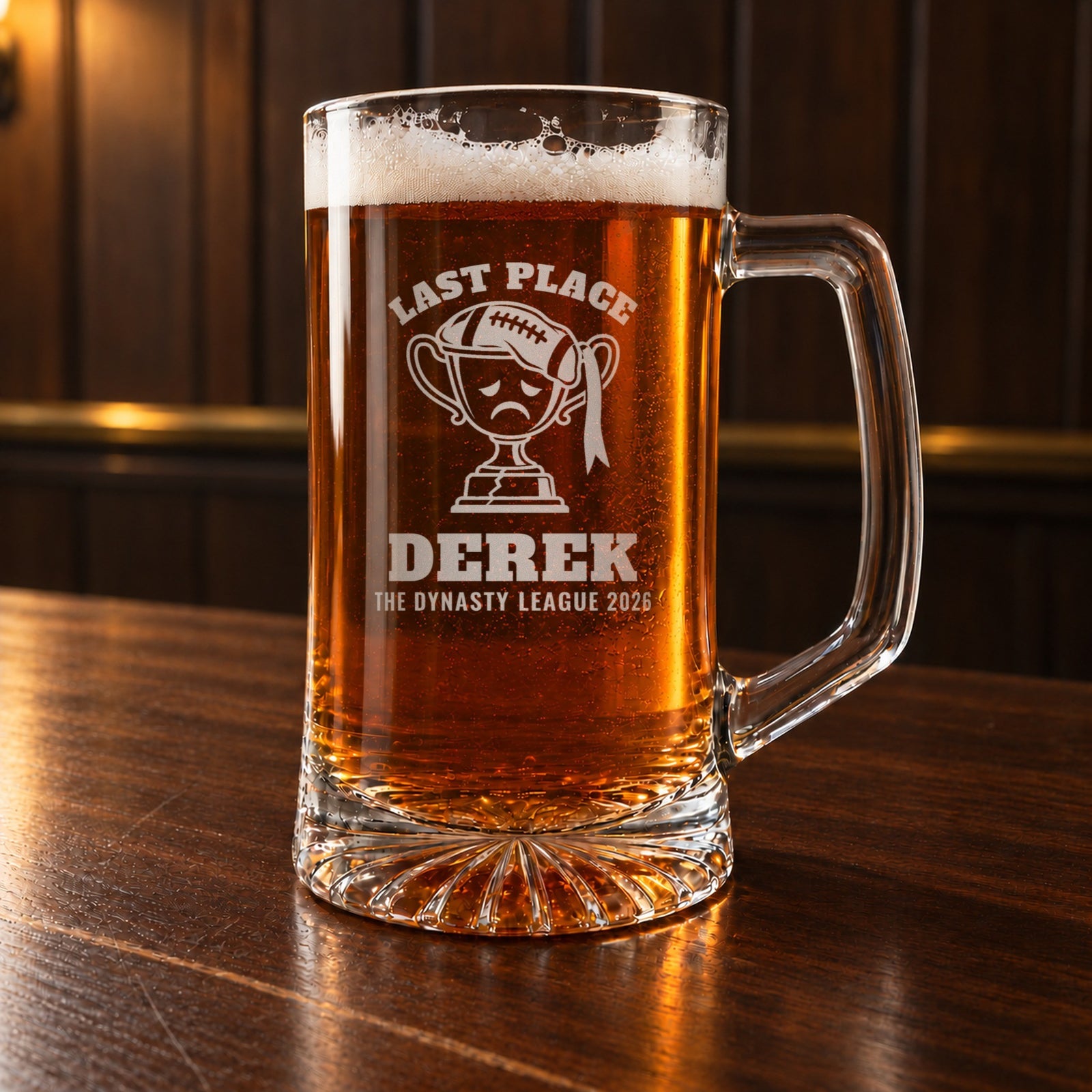 Fantasy football last place beer stein on a bar, engraved with a sad trophy wearing a flat football, Last Place, Derek and The Dynasty League 2026