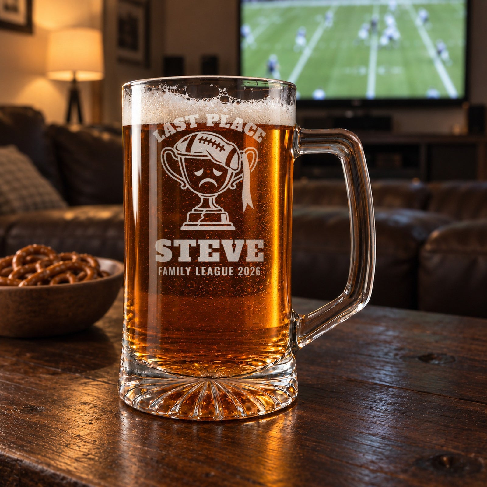 Fantasy football last place beer stein on a man cave coffee table with a football game on TV behind it, engraved Last Place, Steve, Family League 2026