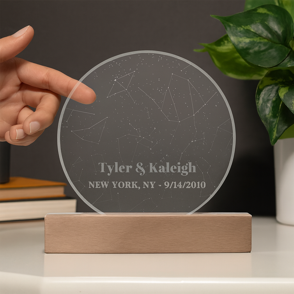 Round acrylic plaque with laser-engraved constellation map and sample personalization reading "Tyler & Kaleigh NEW YORK, NY - 9/14/2010" mounted on natural wood base