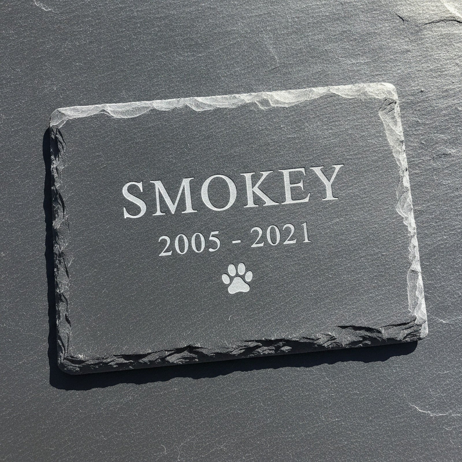 Close view of the recessed laser engraving on a natural slate pet grave marker, the sample name Smokey cut pale into the dark stone surface