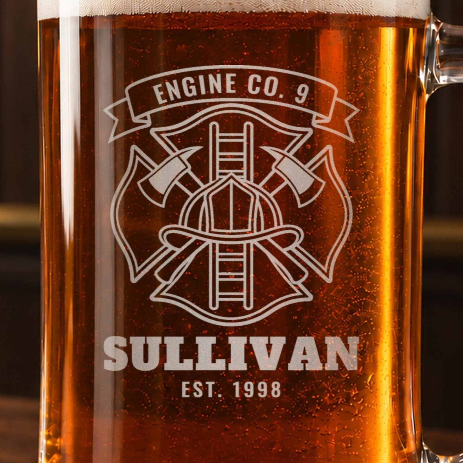 Close-up of the frosted Maltese cross engraving on a firefighter stein: helmet, crossed axes and ladder, Engine Co. 9, Sullivan and Est. 1998