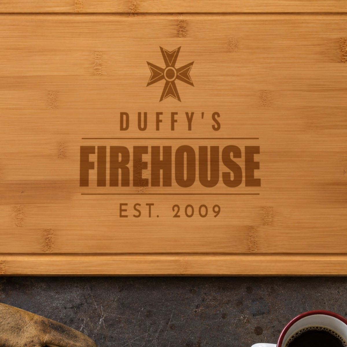Close-up of the laser engraving on the firehouse cutting board: the Maltese cross, DUFFY'S and FIREHOUSE burned into the bamboo grain