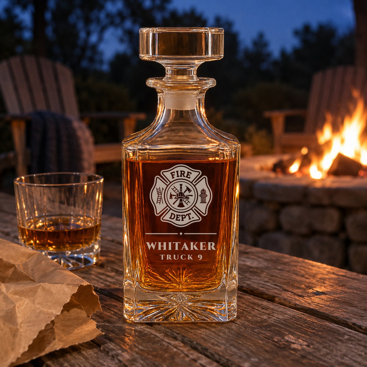 Personalized firefighter decanter engraved Whitaker, Truck 9, on a backyard table by the fire pit with a rocks glass and torn kraft paper