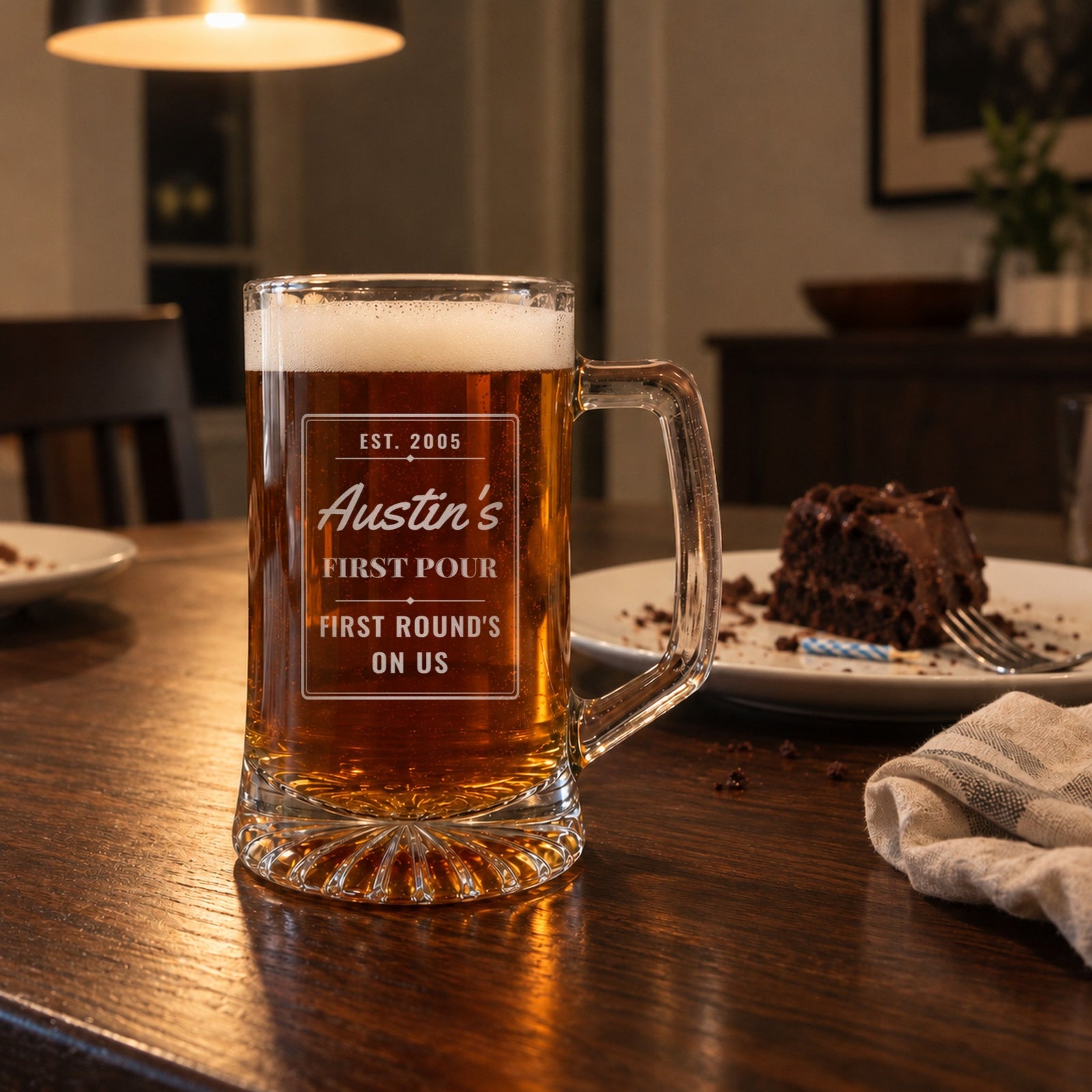 Personalized 21st birthday beer stein on a dinner table beside birthday cake, engraved for Austin with First Round's on Us, a gift from his friends