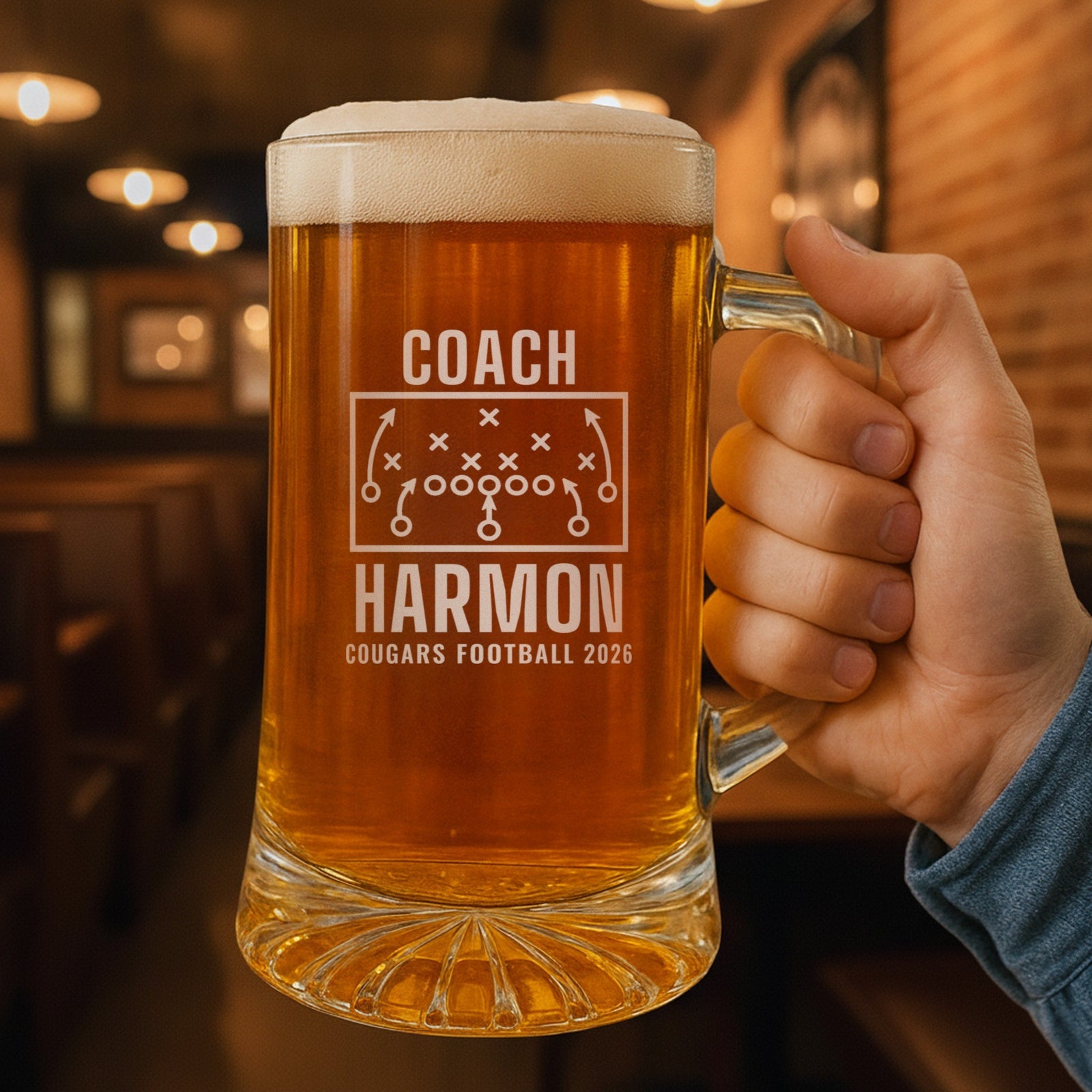Hand holding the 25 oz personalized football coach playbook beer stein in a pub, engraved with a football play diagram with X's, O's and routes: Coach, Harmon