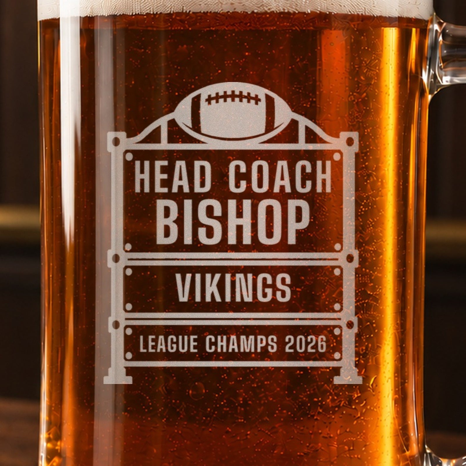 Close-up of the frosted engraving on the football coach scoreboard beer stein, a vintage stadium scoreboard with a football on top: Head Coach, Bishop, Vikings, League Champs 2026