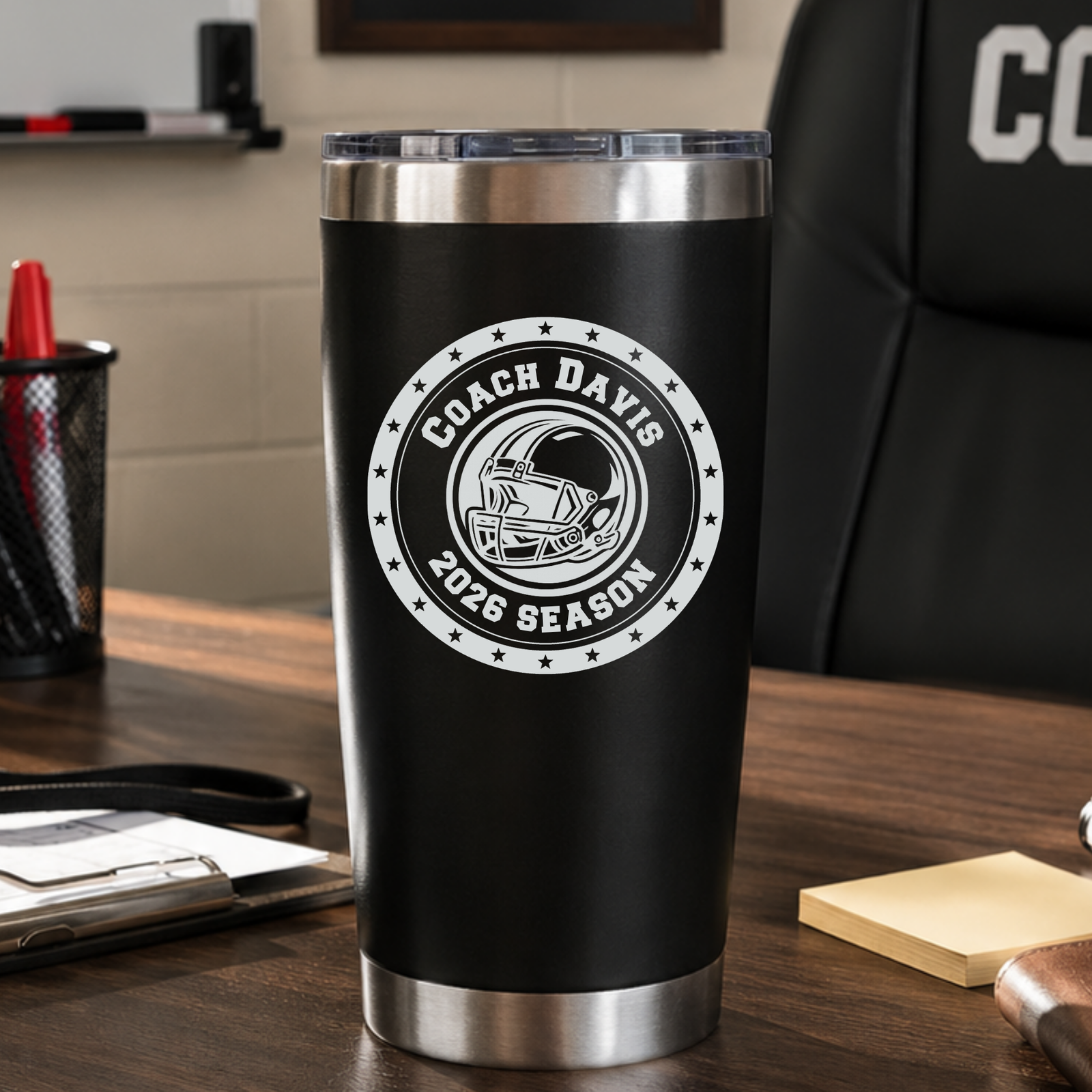 Black football coach tumbler engraved with COACH DAVIS and 2026 SEASON, sitting on a coach's desk, a personalized end-of-season gift