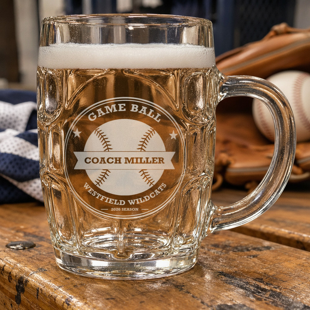 Personalized baseball coach beer stein on a locker room bench beside a glove and ball, frosted engraving reading Game Ball, Coach Miller and Westfield Wildcats