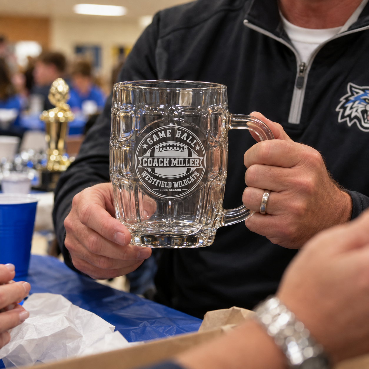 Football coach holding his engraved Game Ball beer stein at an end-of-season team banquet, personalized with Coach Miller and Westfield Wildcats