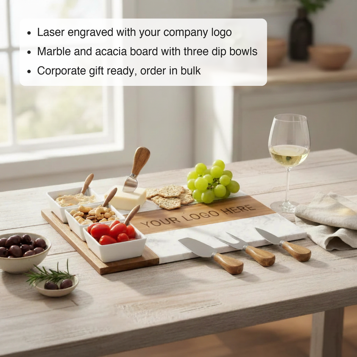 Custom logo marble charcuterie board feature view engraved with a Your Logo Here sample, three filled dip bowls, cheese, crackers, and wine on a bright kitchen table.