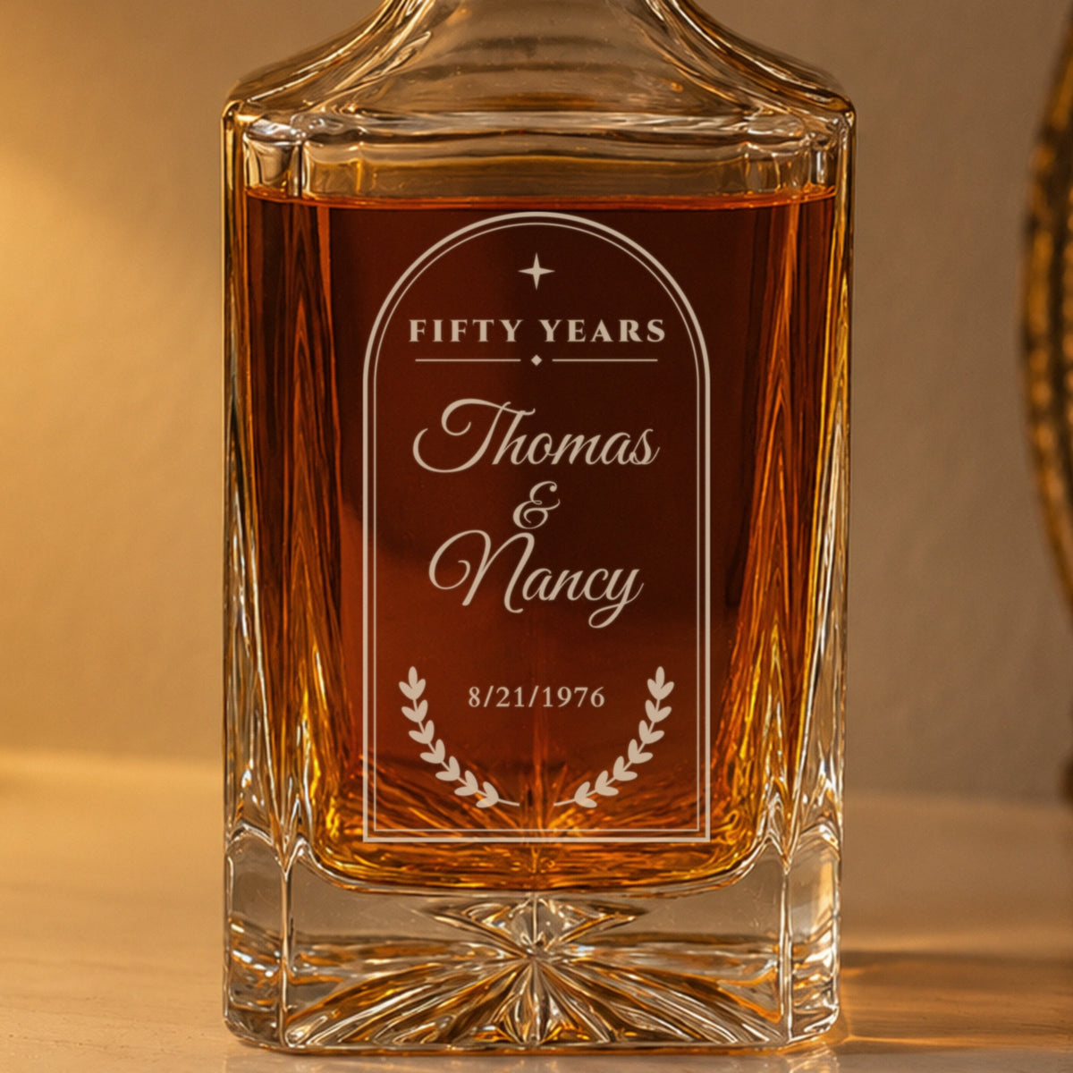 Close-up of the frosted laser engraving on a 50th anniversary decanter: arched frame, Fifty Years, Thomas and Nancy in script, laurel and 8/21/1976