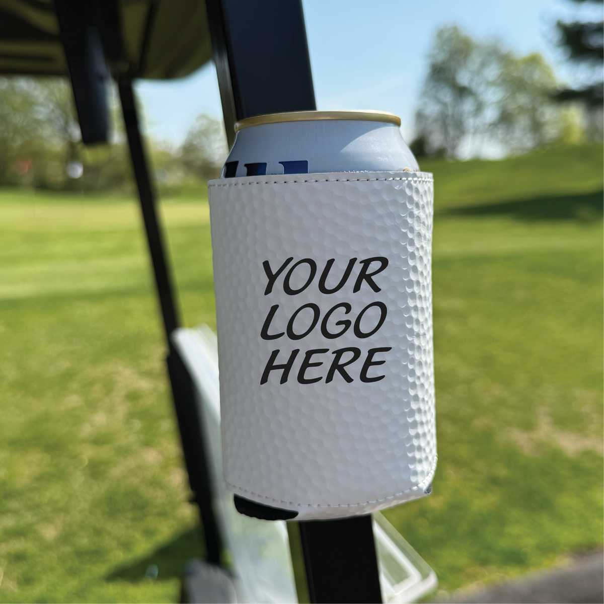 White golf ball-textured can cooler with magnetic backing attached to golf cart rail, displaying sample logo placeholder text in outdoor course setting