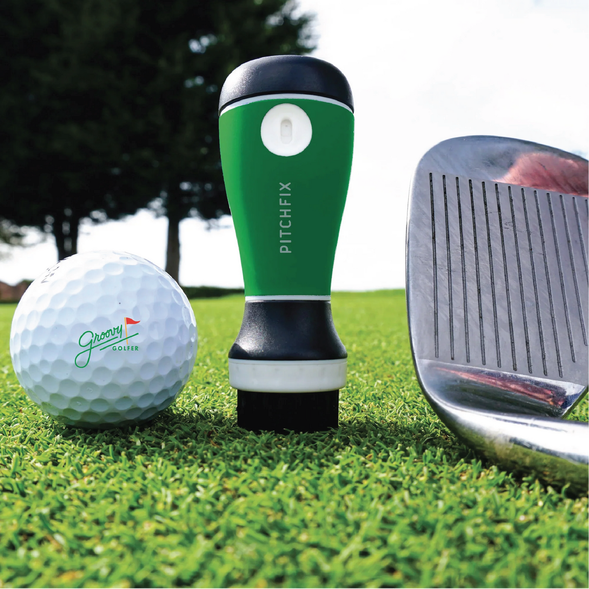 Green AquaBrush golf club cleaner from the golfer's gift box, standing on the green beside a branded golf ball and an iron.