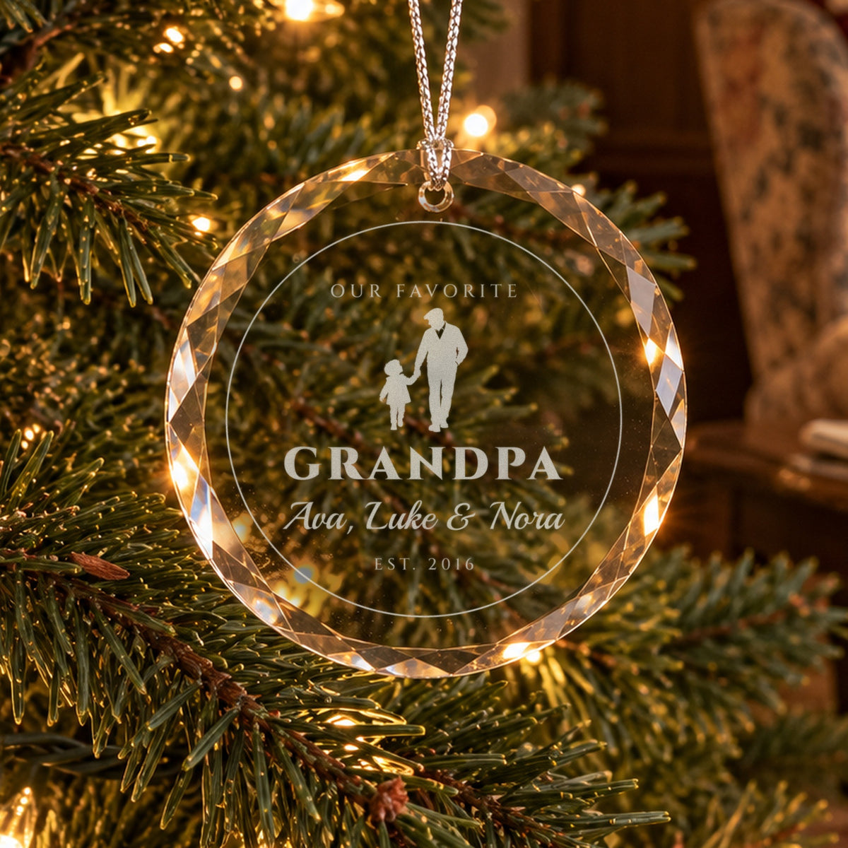 Personalized grandpa Christmas ornament in faceted glass on a lit tree, engraved with a grandfather and grandchild holding hands, OUR FAVORITE GRANDPA, Ava, Luke & Nora, EST. 2016
