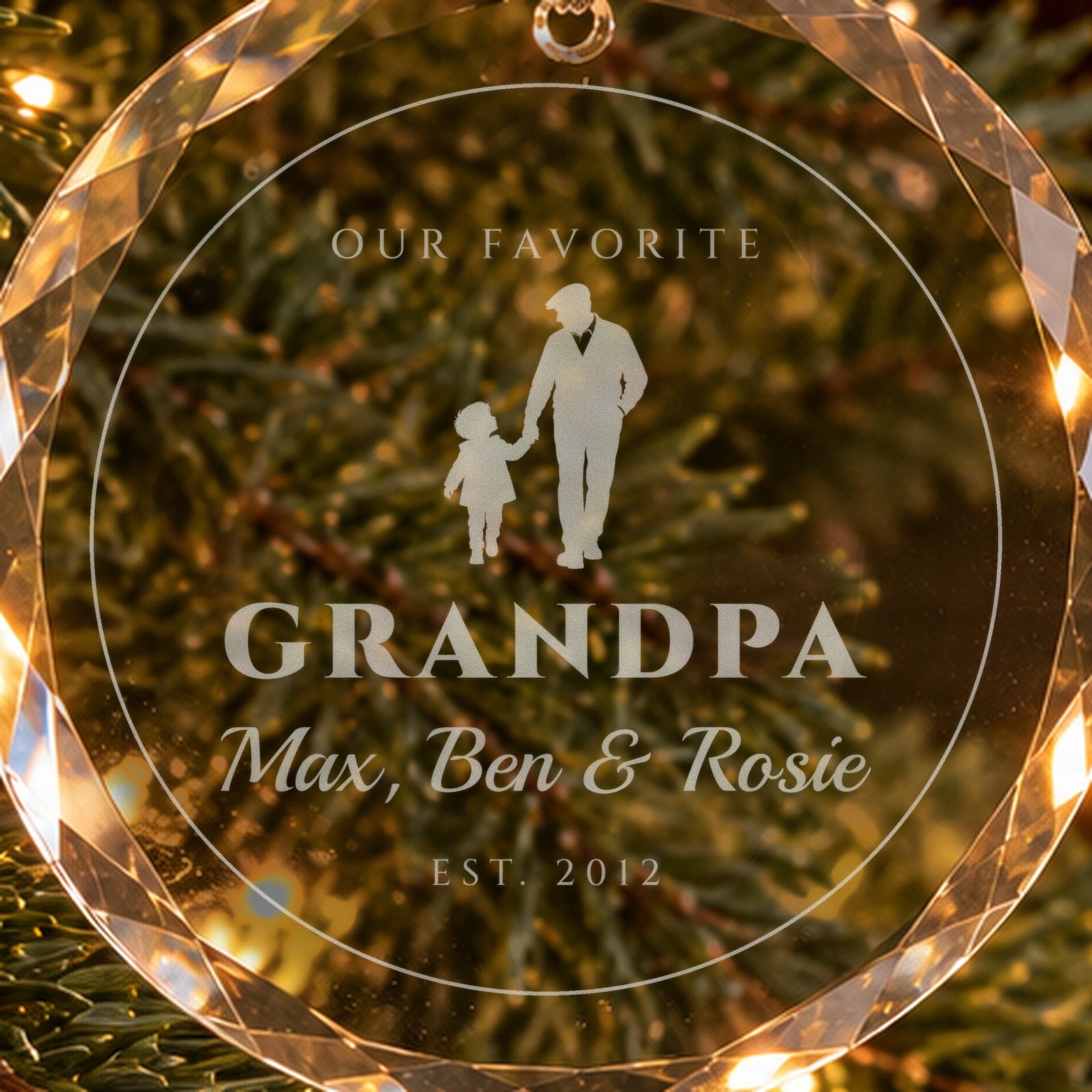 Close-up of the frosted engraving on the grandpa ornament: a grandfather walking hand in hand with a grandchild, GRANDPA, Max, Ben & Rosie, EST. 2012
