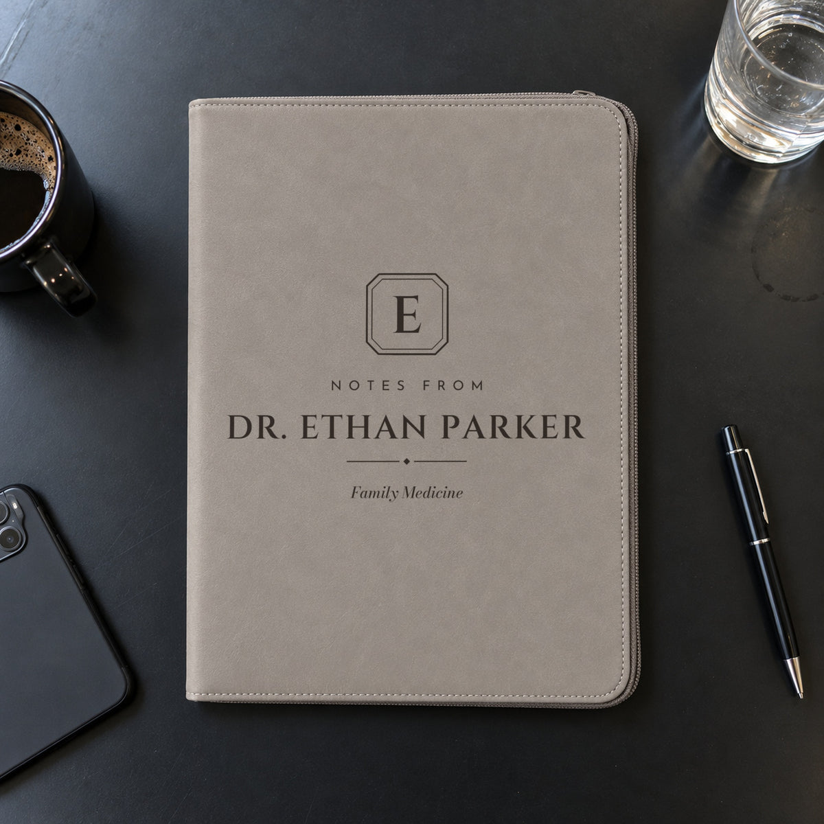 Gray monogram padfolio engraved Notes from Dr. Ethan Parker, Family Medicine, on a black conference table with a coffee cup